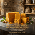 Golden turmeric soap bars stacked beside turmeric roots, powder and green leaves on a worktop in a rustic setting.